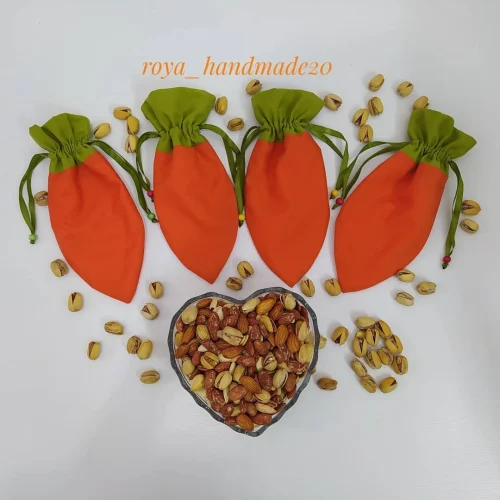 چهار کیسه پارچه‌ای هویجی نارنجی با دهانه‌ی سبز، دور ظرف قلبی پر از آجیل