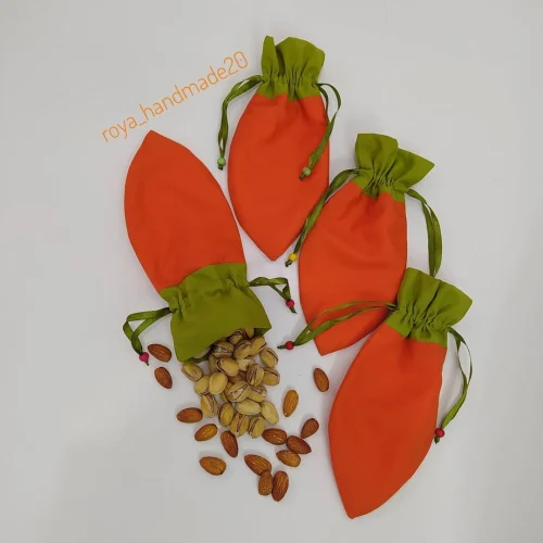 کیسه پارچه ای هویجی نارنجی با دهانه‌ی سبز و بند ساتن، چهار عدد کنار پسته و بادام