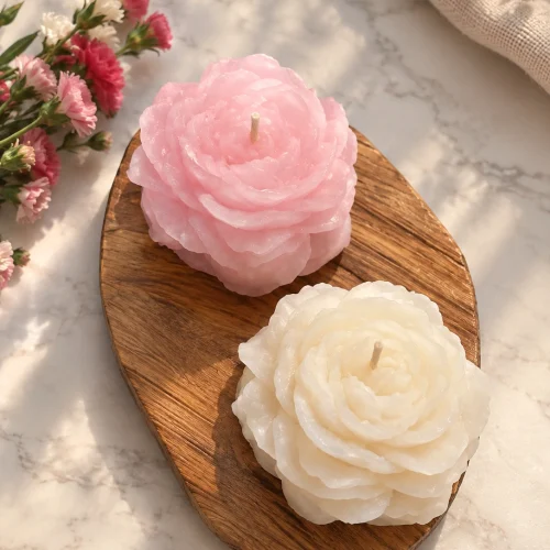 دو شمع دست‌ساز طرح آلاله به رنگ صورتی و سفید روی تخته‌ی چوبی، کنار گل‌های صورتی